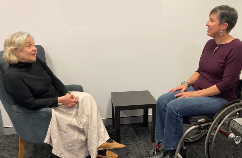 Two women sitting and talking with each other. One woman is in a wheelchair.