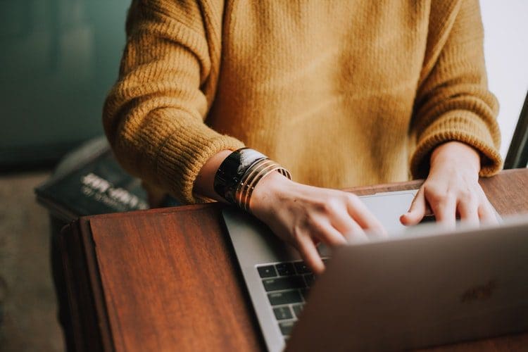 women in a tan coloured jumper working on a silver laptop