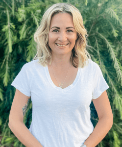 A portrait of a blonde woman smiling against a garden backdrop.